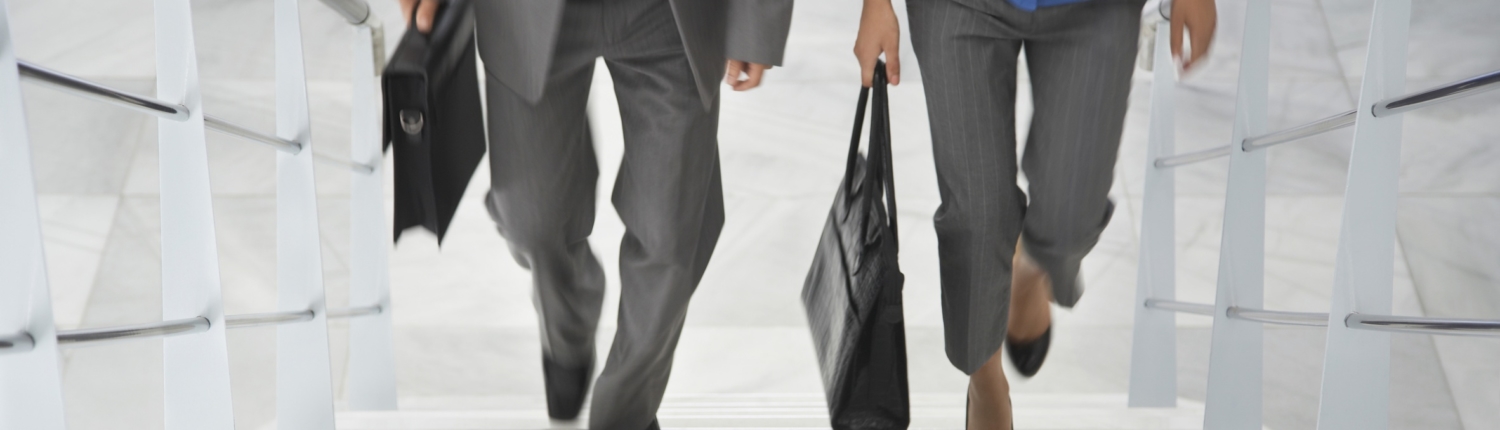Lowsection of two businesspeople walking up stairs with bags in office